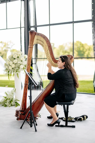 Maia Wachter- Harpist playing prelude music at a wedding ceremony beside white floral arrangements