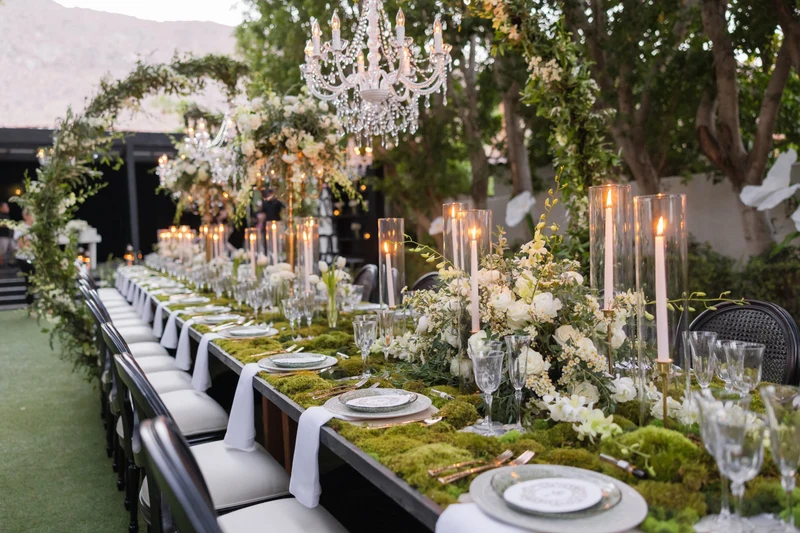 Artisan Event Floral Decor long reception table with greenery garland, moss runner and white florals under a chandelier