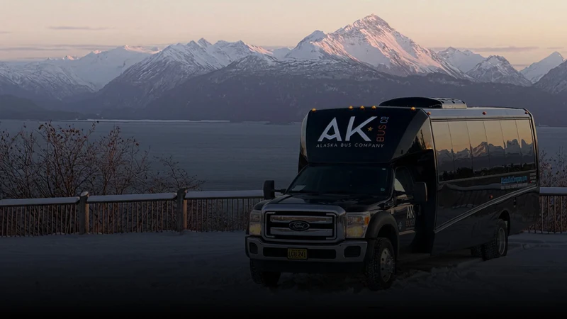 Alaska Bus Company luxury bus parked above a bay with snow covered mountains at sunset