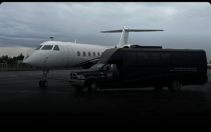 Alaska Bus Company charter bus parked beside a private jet on an airport tarmac