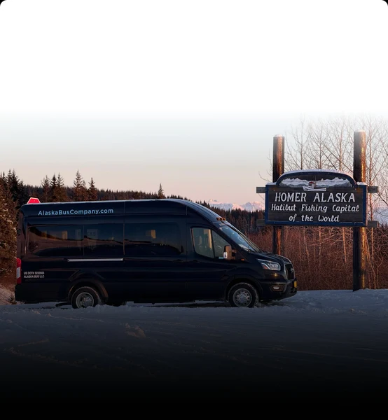 Alaska Bus Company passenger van beside the Homer, Alaska welcome sign in winter