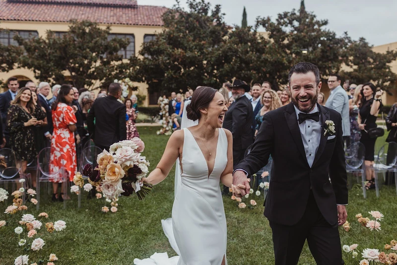 Events Inspired couple walking back up a flower-lined aisle on a lawn
