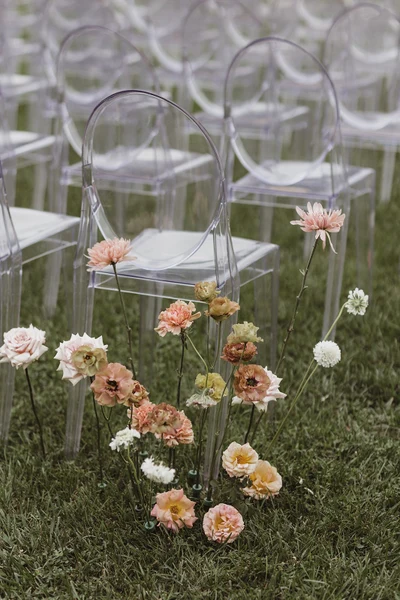 Events Inspired aisle florals beside clear chairs on a lawn
