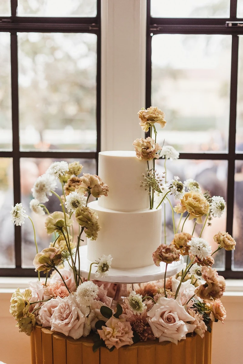 Events Inspired three-tier wedding cake surrounded by blush and peach florals