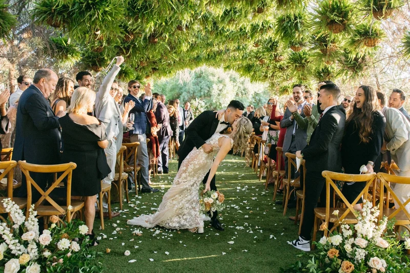 Khoa Photography newlyweds kissing in the aisle as guests cheer at a garden ceremony