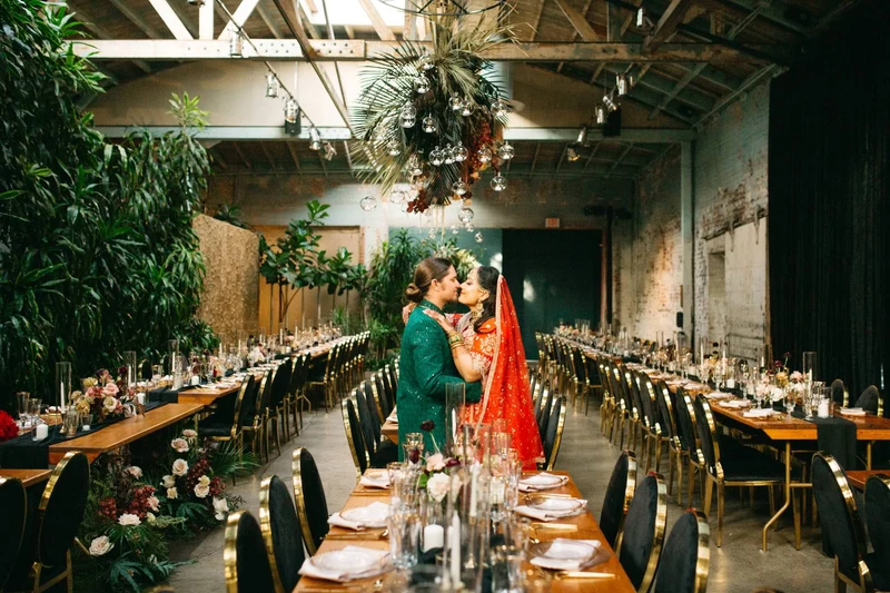 Khoa Photography couple kissing between long reception tables in a hall filled with greenery
