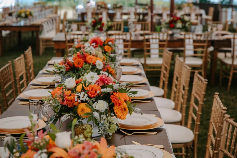 Folls' Flowers centerpieces along a long farm table under a reception tent