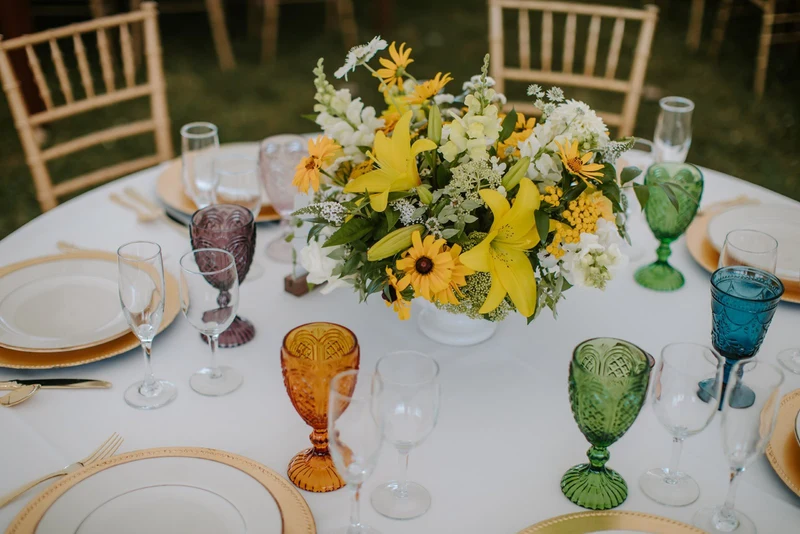 Folls' Flowers yellow centerpiece with lilies on a round table set outdoors