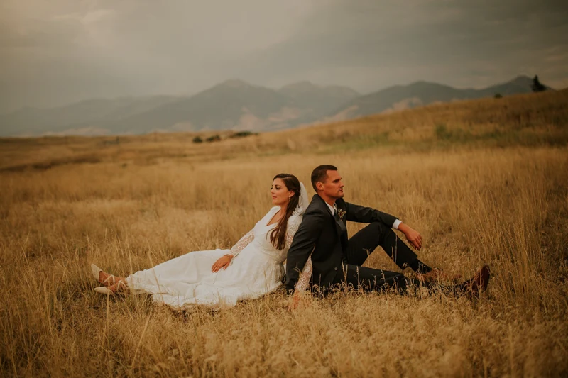 Addie Fath Photography bride and groom sitting back to back in a golden field below mountains