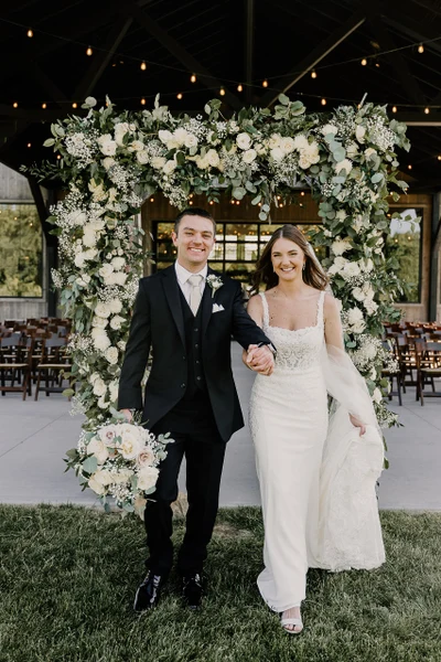 Rose's Bouquets full white and green floral arch behind a couple at an outdoor wedding