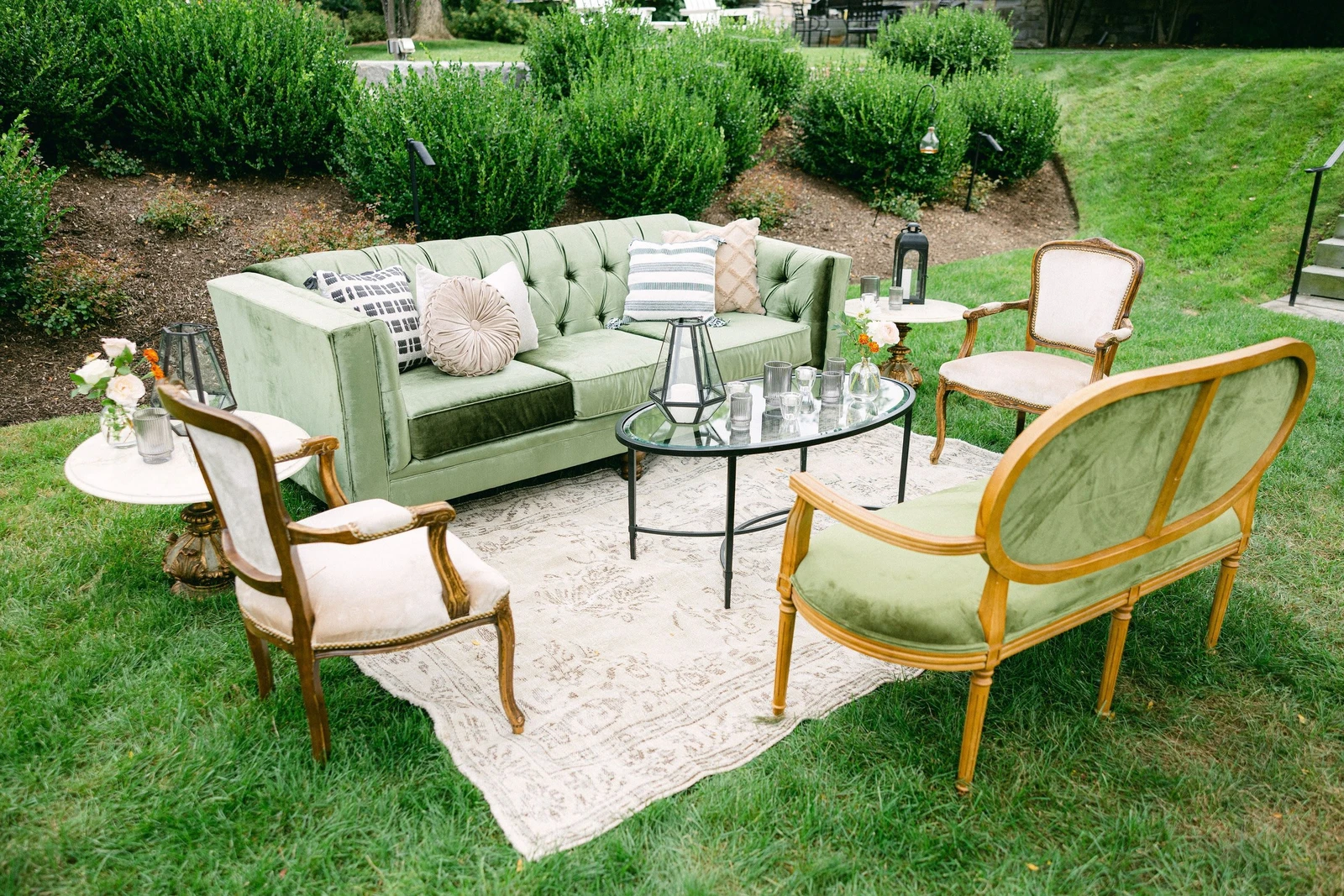 She Rents Vintage lounge on a lawn with a green velvet sofa, cane settee, armchairs and a patterned rug