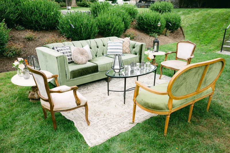 She Rents Vintage lounge on a lawn with a green velvet sofa, cane settee, armchairs and a patterned rug
