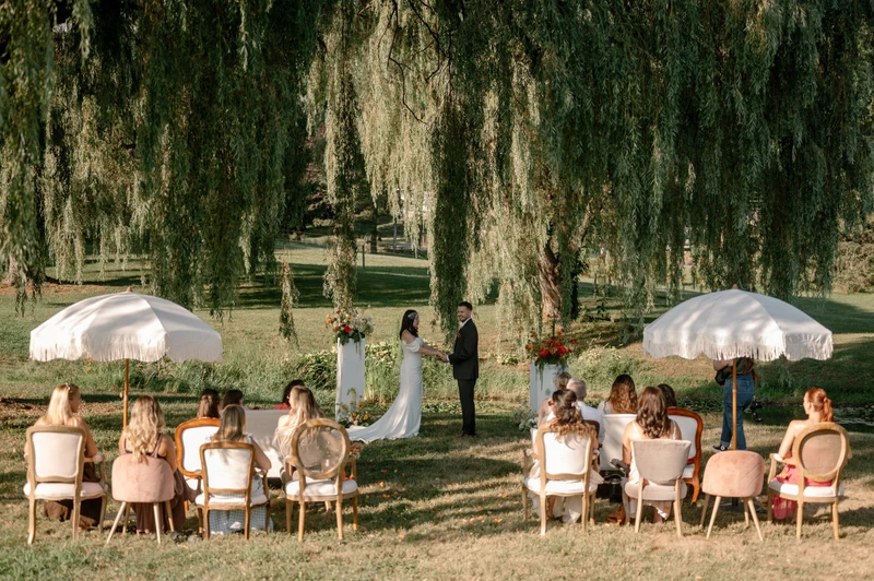 She Rents Vintage ceremony seating and fringed umbrellas under a willow tree