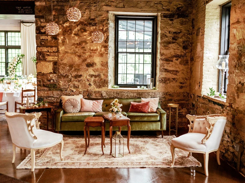 She Rents Vintage lounge with a green velvet sofa and cream armchairs against a stone wall