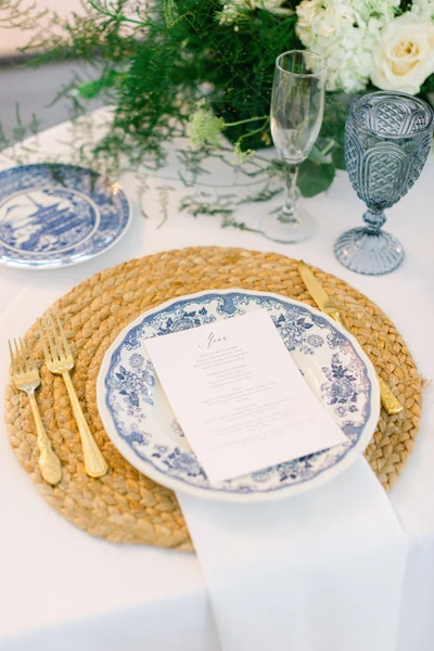 She Rents Vintage place setting with blue and white china, gold flatware and a woven charger