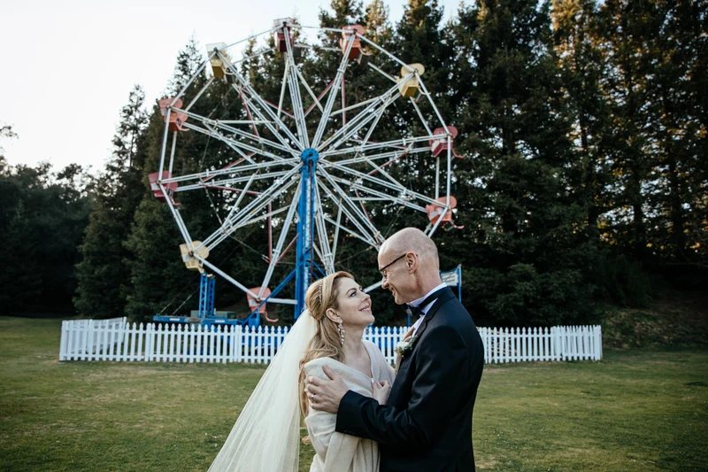 LEAF Wedding Photography bride and groom embracing in front of a ferris wheel and pine trees