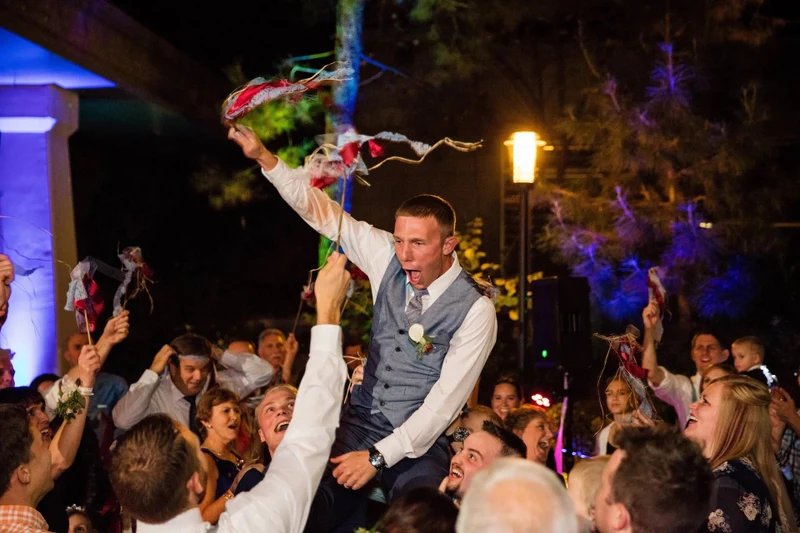 Sound Prodigy guests lifting the groom on a chair at an outdoor evening reception with colored uplighting
