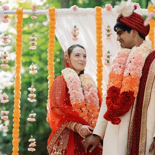 Crown Coordination couple wearing flower garlands under a marigold draped canopy at an outdoor ceremony