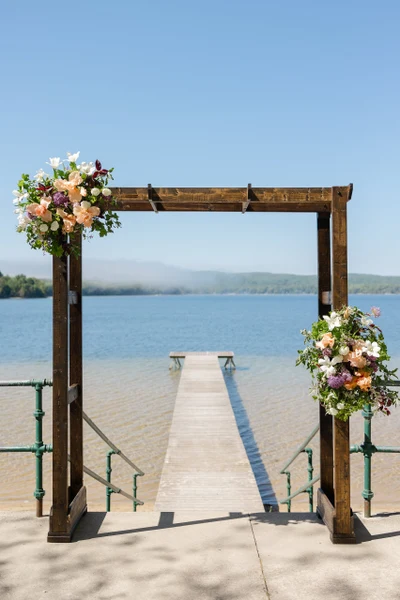 Moondance Flower Farm wooden lakeside wedding arch decorated with colorful seasonal flowers overlooking the water