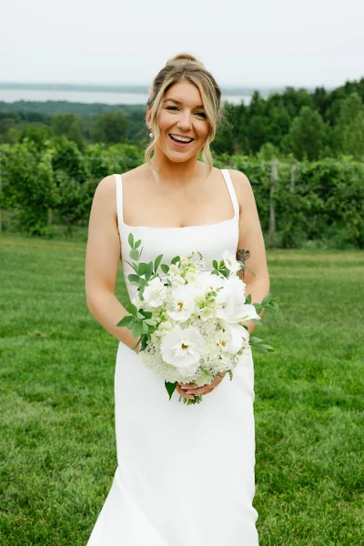 Moondance Flower Farm bride holding a lush white and green seasonal wedding bouquet with vineyard and water views in Northern Michigan