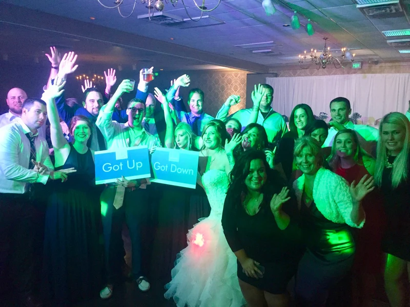 Get Up to Get Down Elite Entertainment bride and guests posing with party signs on a dance floor in green and blue light