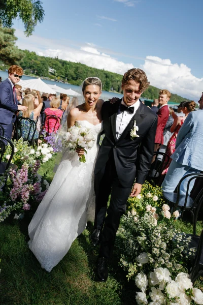 Anna Beth Smith couple walking back up a flower-lined aisle after an outdoor lakeside ceremony