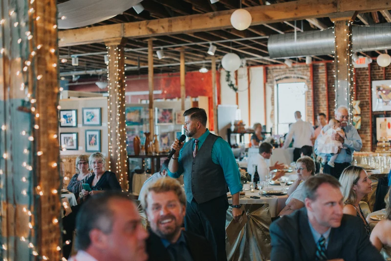 A+ Entertains emcee with a microphone during a reception in a brick loft