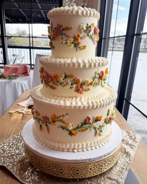 Sugar Blossom Cake Shop three-tier wedding cake with piped buttercream flowers beside a waterfront window