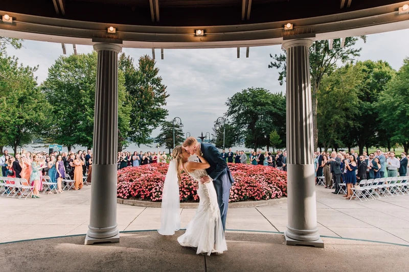 Brittany Juravich Photography bride and groom kissing under a pavilion with wedding guests and a flower garden behind them