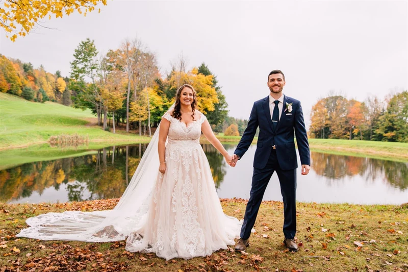 Brittany Juravich Photography couple holding hands beside a pond ringed with autumn trees