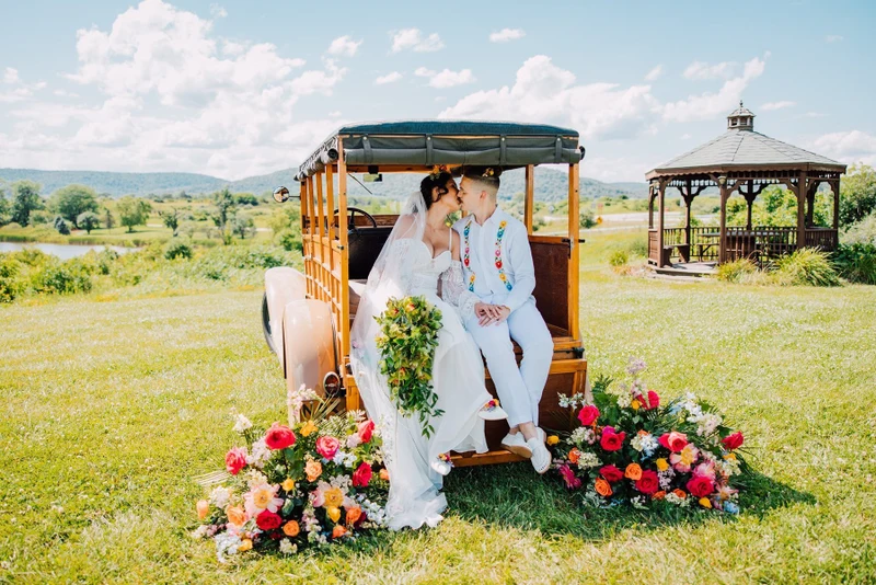 Brittany Juravich Photography newlyweds kissing on the back of a vintage wood-sided truck in a field, with bright flowers at their feet