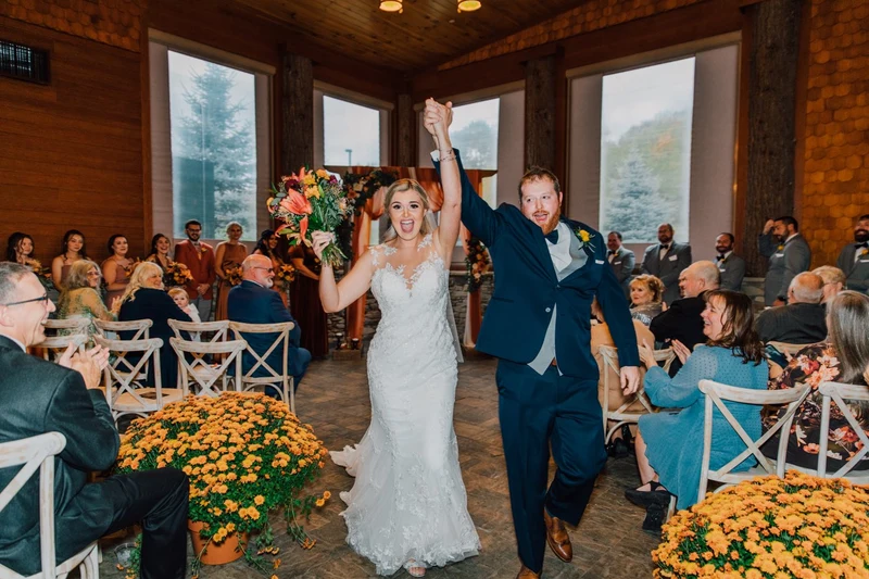 Brittany Juravich Photography bride and groom cheer while walking down the aisle after a fall wedding ceremony with mums lining the aisle