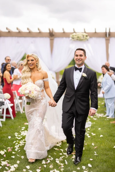 RD Events & Design newlyweds walking up a petal-strewn lawn aisle away from a draped pergola