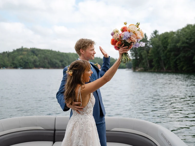 Bittersweet & Co. bride raising a bright bouquet on a boat on the lake