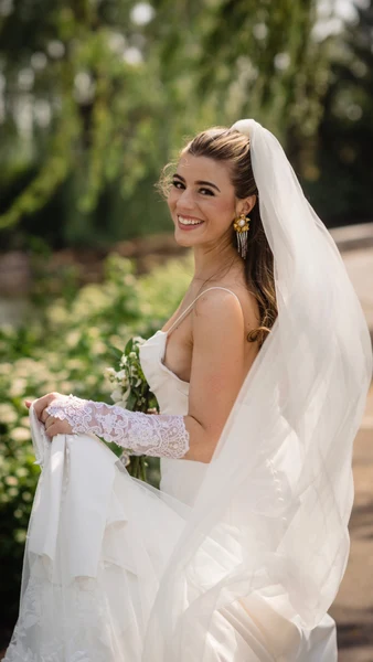 J.Luxe Salon bride with hair swept back under a long veil, smiling in a garden