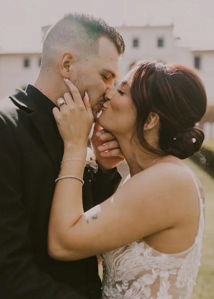 J.Luxe Salon bride with a low pinned updo kissing the groom outdoors