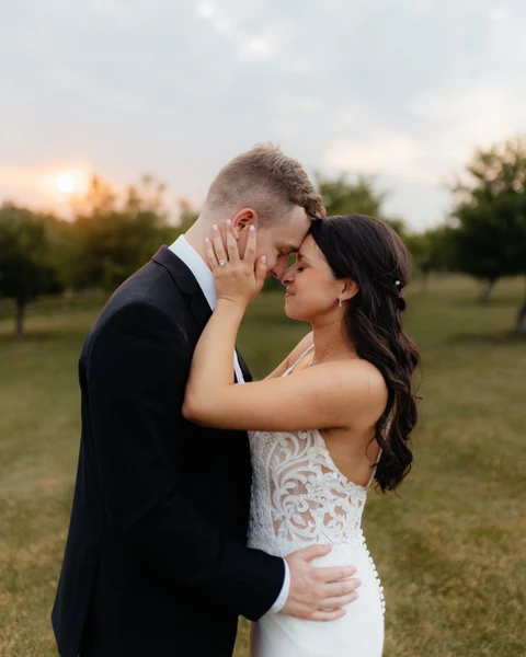 J.Luxe Salon bride with long waves and a hair clip, embracing the groom in a field at sunset