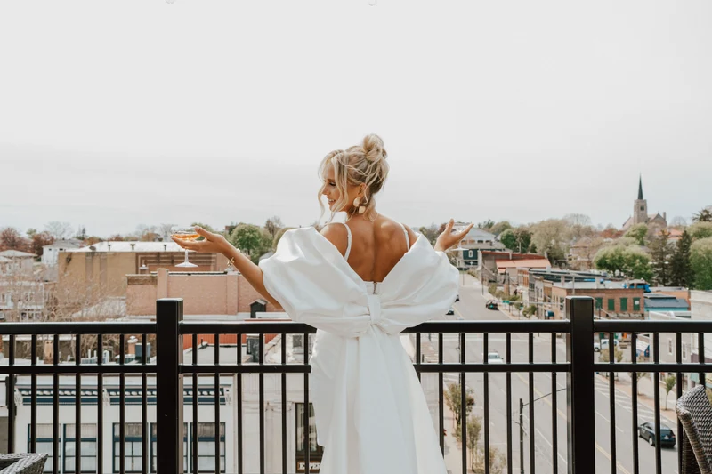 J.Luxe Salon bride with a high bun raising a glass on a balcony above a small town