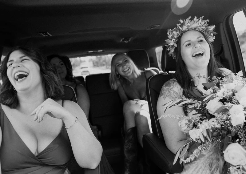 Michael Murphy IV Photography black and white photo of a bride in a flower crown laughing with bridesmaids in a car