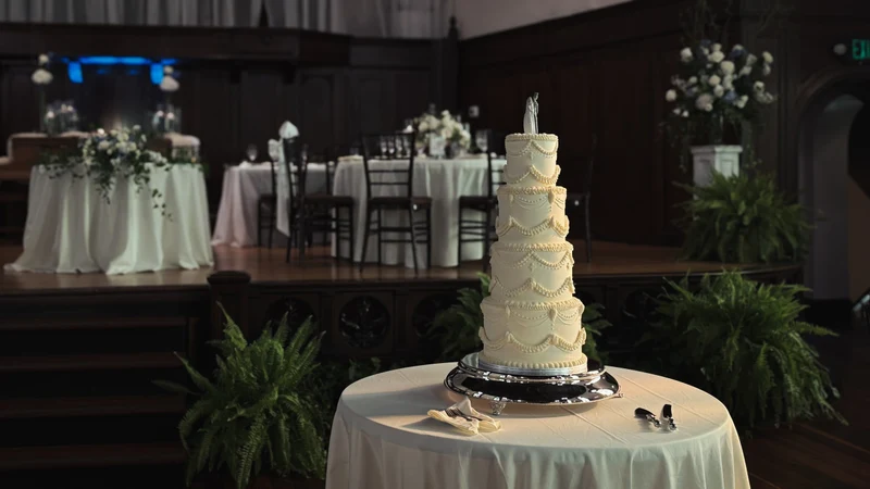 Butter & Batter Bakery four-tier wedding cake with vintage piping on a draped table in a reception hall