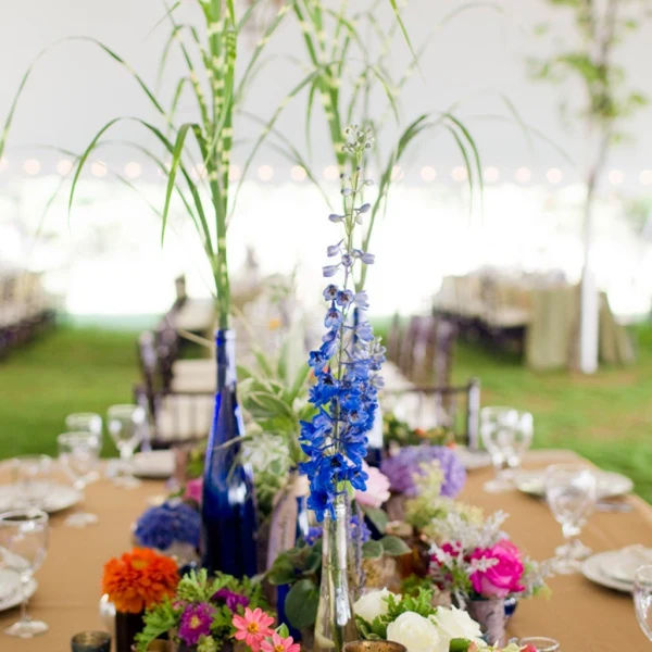 Amy Kate Designs centerpiece with blue delphinium and garden flowers on a long table under a tent