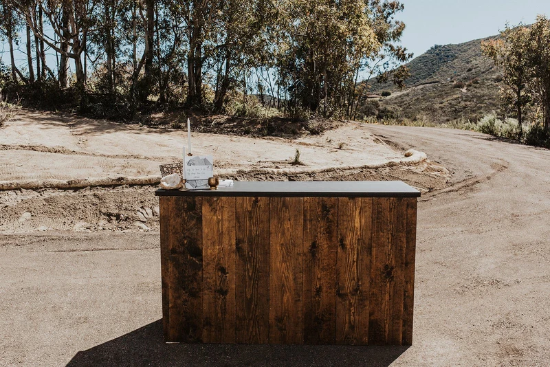 Wonder Event Rentals rustic wood bar set up outdoors on a hillside property