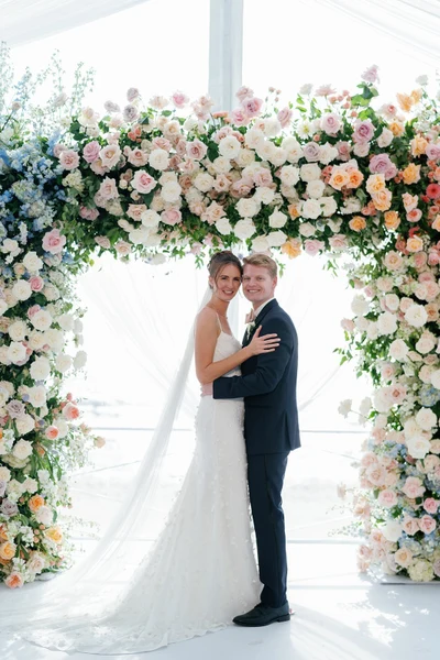 Conradie Event Design couple under a pastel floral arch inside a draped white tent