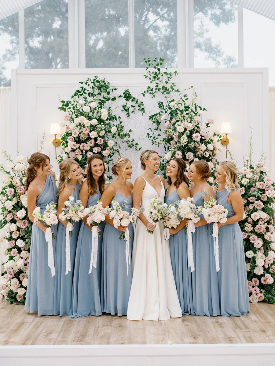 Conradie Event Design bride and bridesmaids in blue dresses holding bouquets before a floral arch