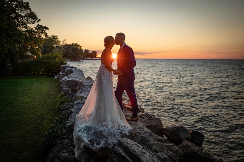 Jeffrey Foote Photography couple kissing on a rocky lakeshore beside a lawn at sunset