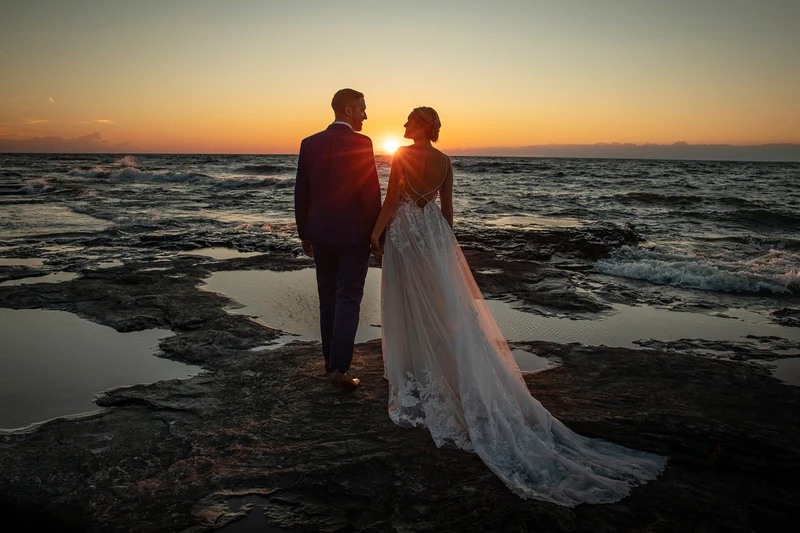 Jeffrey Foote Photography bride and groom silhouetted on a rocky lakeshore at sunset