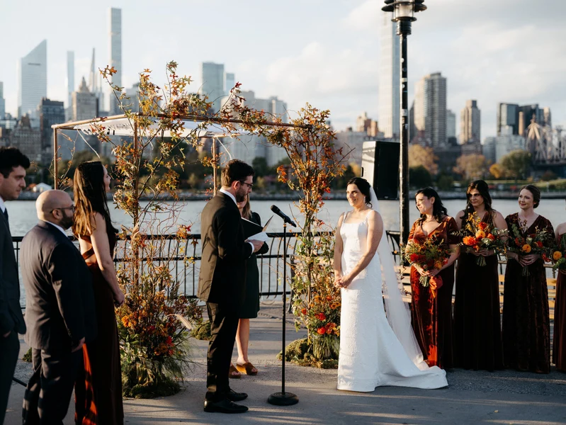 Wilder Gardens + Flowers ceremony arch of autumn branches and flowers at a waterfront wedding with a city skyline behind