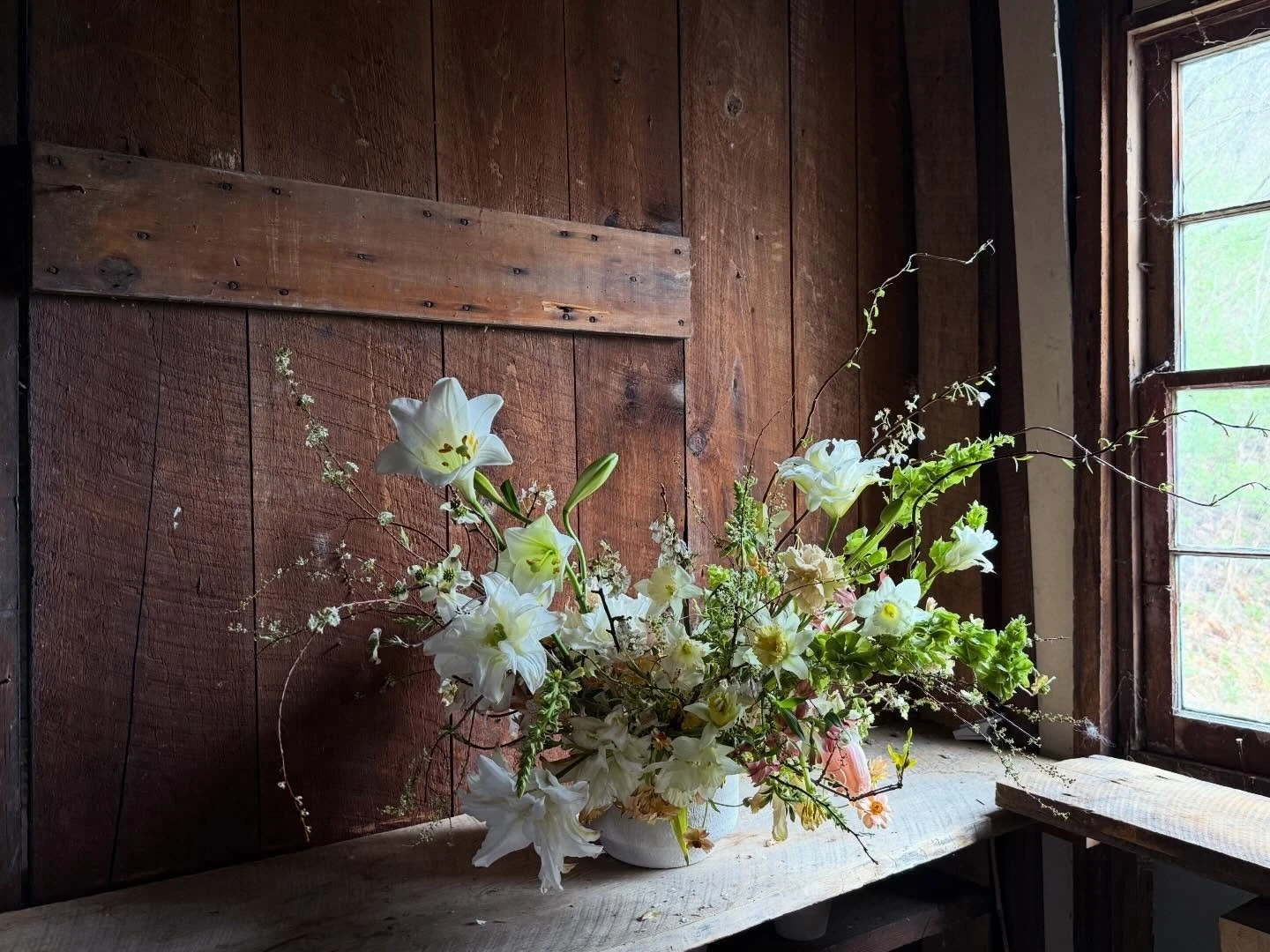 Wilder Gardens + Flowers arrangement of white lilies and spring branches against a weathered barn wall