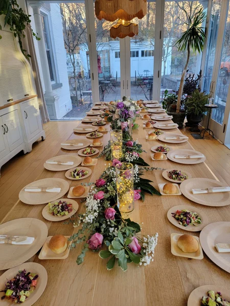 Ba-Li Cravings long table set with salads, bread rolls and a floral runner in a sunroom