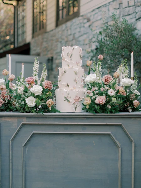 LILA Cake Shop three-tier floral wedding cake displayed outdoors among fresh flowers and candles